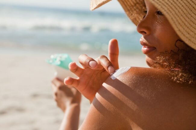 Young attractive woman attentively applying sunscreen on her sho