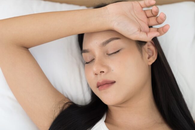 Young Asian woman sleeping on bed and keeping eyes closed while covered with blanket in bedroom. Asian woman sleep and lying on bed in bedroom in the morning. Healthcare concept