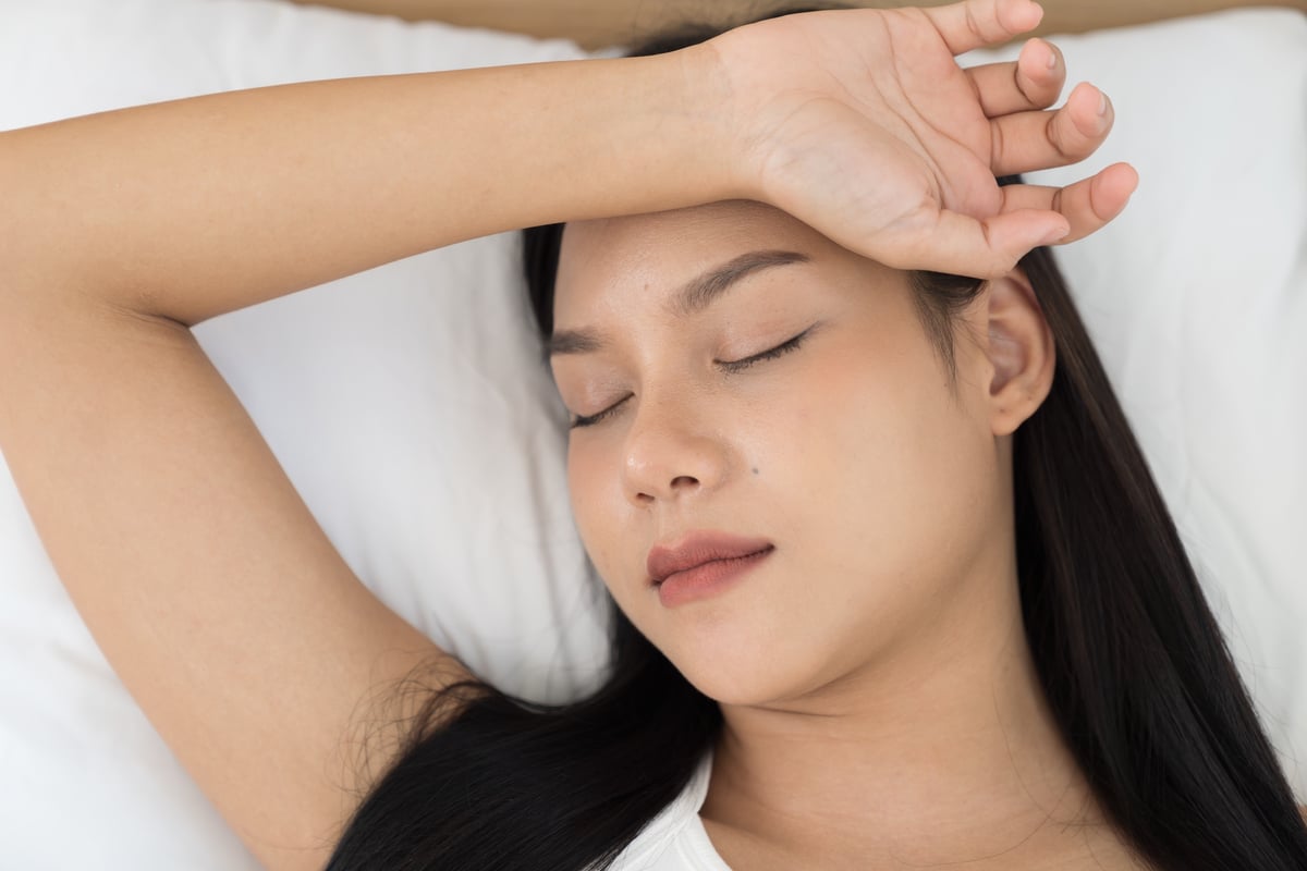 Young Asian woman sleeping on bed and keeping eyes closed while covered with blanket in bedroom. Asian woman sleep and lying on bed in bedroom in the morning. Healthcare concept