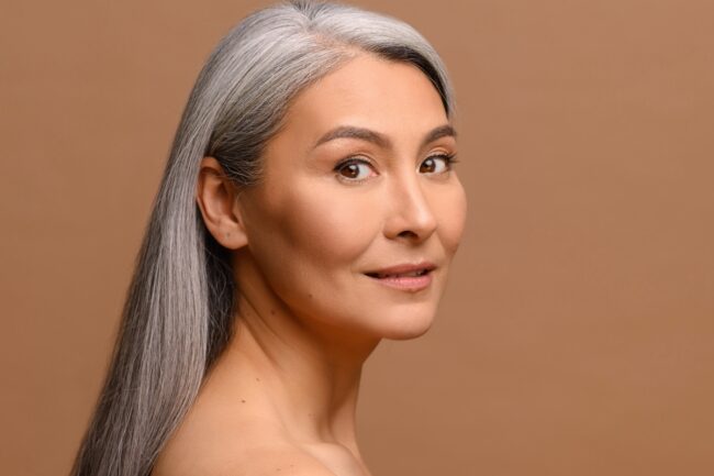 Headshot beautiful middle-aged Asian woman with fresh clean healthy skin isolated on beige